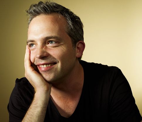 Author Matt Brown, who wrote the Compton Valance books. A young man with light brown hair, wearing a black t-shirt and leaning on one hand while smiling. 