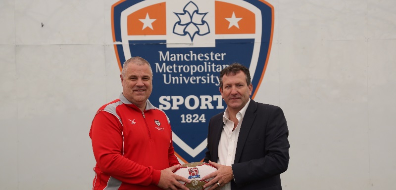 Representatives from Manchester Metropolitan University and Toronto Wolfpack pose with a rugby ball in front of the MMU Sport logo