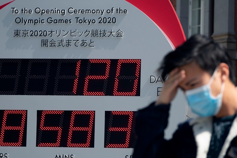 A passer-by in front of the Tokyo 2020 Olympics countdown clock following the postponement announcement due to coronavirus crisis.  Pic: Fiers / Shutterstock.com