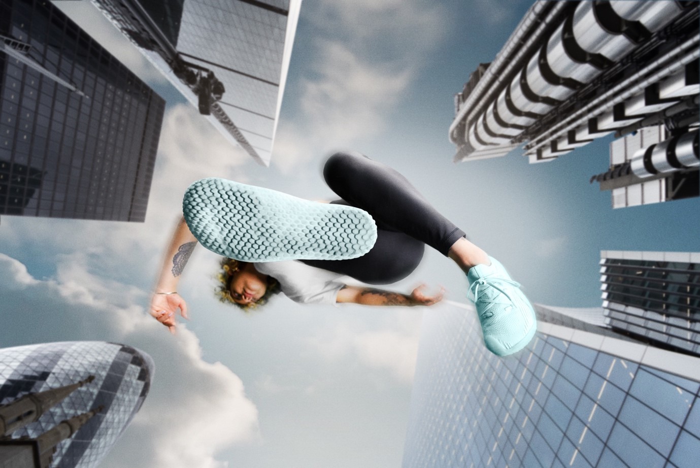 Woman jumping in the air wearing turquoise trainers in the backdrop of silver skyscrapers 