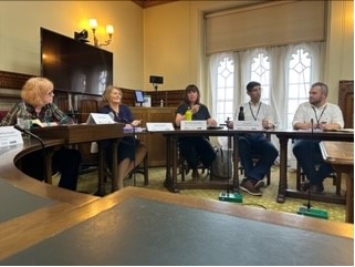 A small team of people, including Hannah Smiths and Paul Gray, are seated around a roundtable participating in discussion