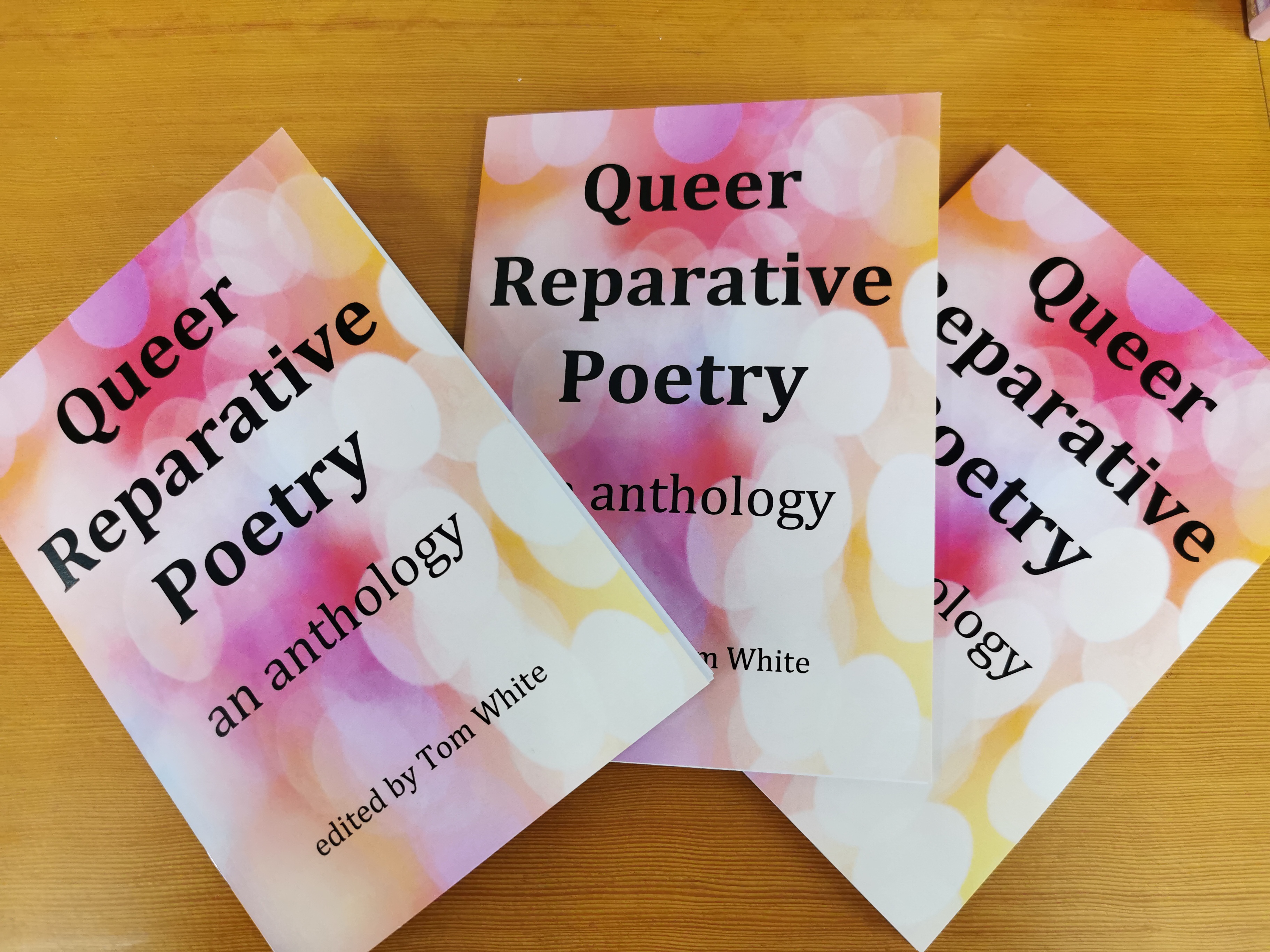 Alt text: Photo shows three copies of Queer Reparative Poetry fanned across a desk