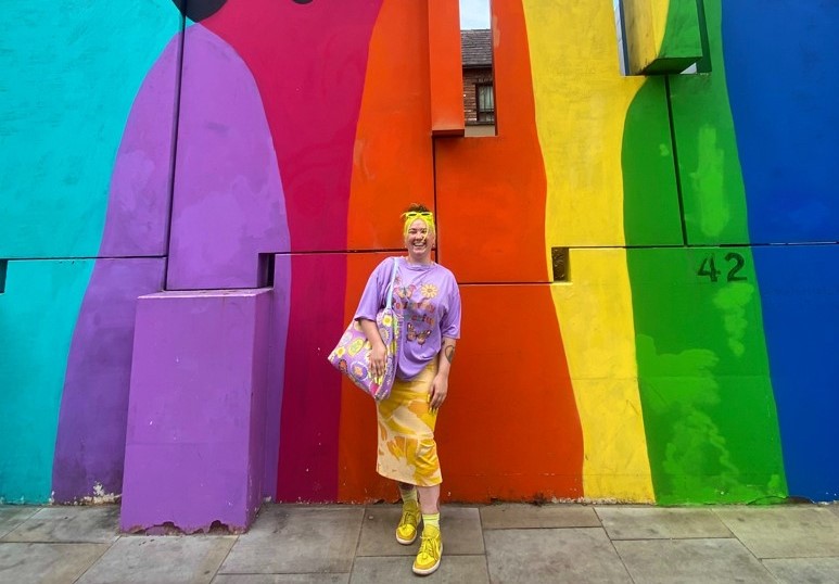 A photo of Kenzye in front of colourful street art.